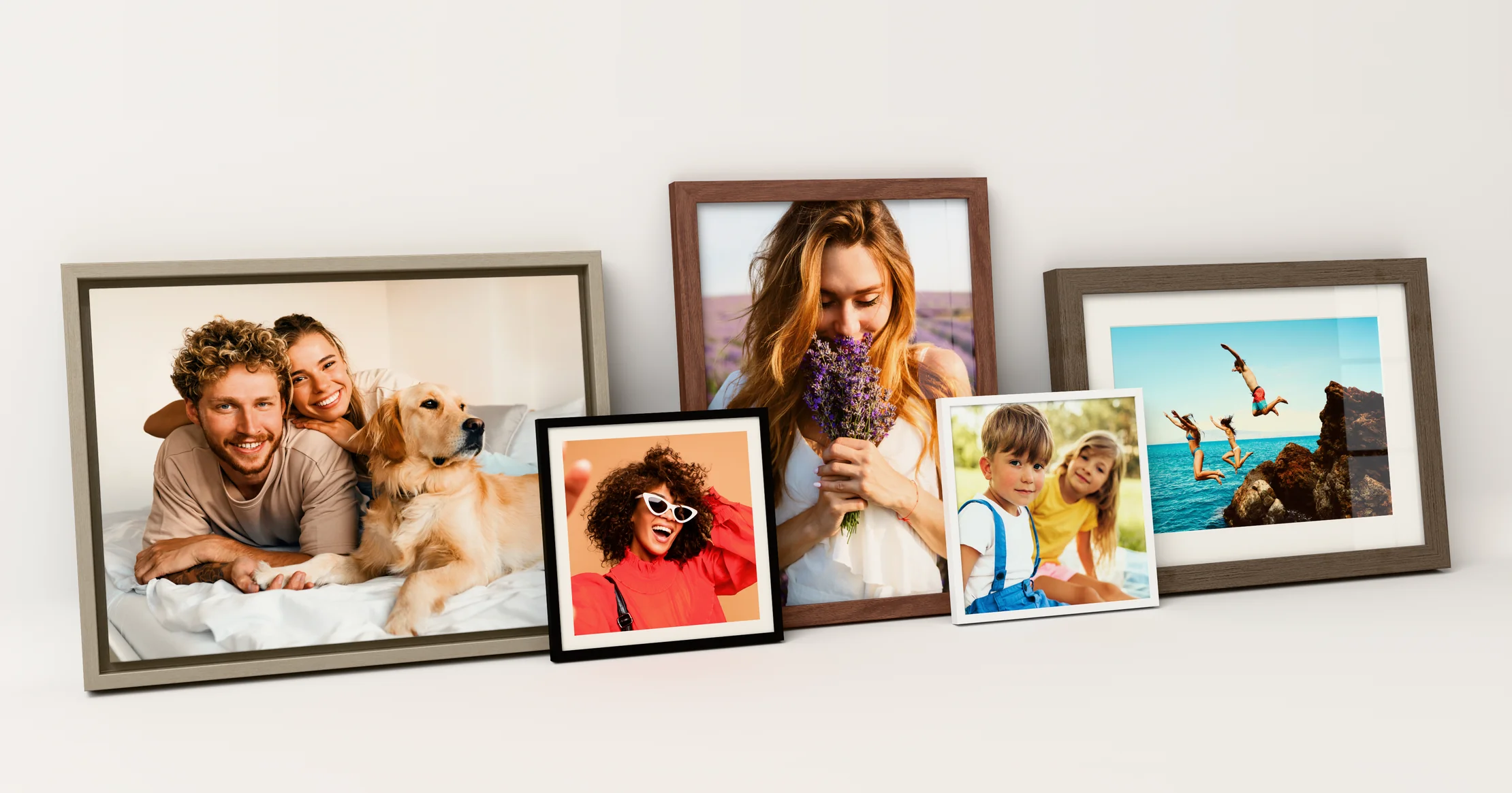 Five framed pieces on a light wall: a canvas in a Vintage silver floating frame, a photo print with a white mat in a Walnut flair frame, a poster in an Oak vintage flair frame, and two photo tiles, one in a Black matte frame with a white paper border and one in a White frame.