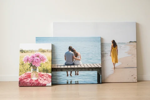 Three landscape photo canvases in different sizes standing side by side against a wall