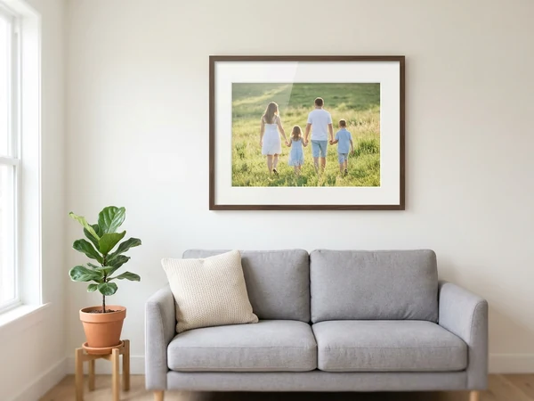 A family photograph printed, mounted and framed in a dark wood frame, hung above a sofa in a living room
