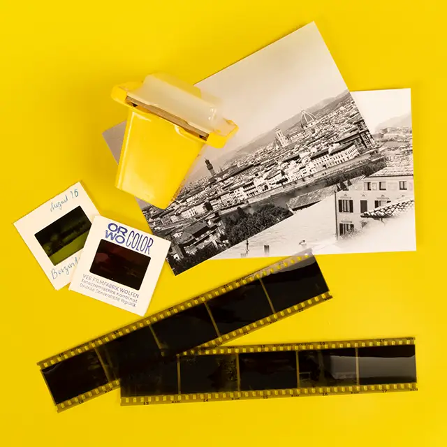 Ein liebevoll arrangiertes Stillleben mit analogen Fotoprodukten: Negativstreifen, gerahmte Dias, klassische Fotoabzüge und ein alter Dia-Betrachter erinnern an die besondere Ästhetik der analogen Fotografie.