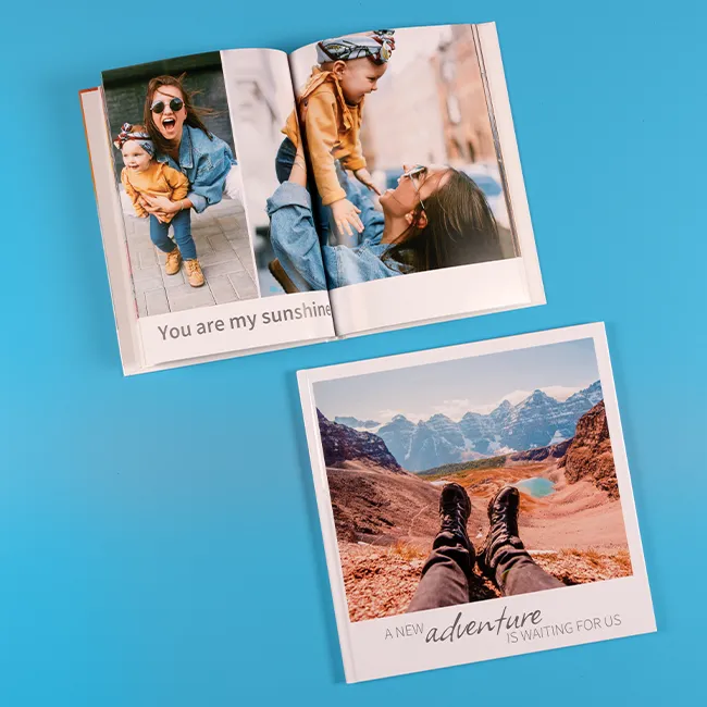 Quadratisches geschlossenes Buch mit Canyonfoto, daneben geöffnetes Fotobuch mit Familienbildern, blauer Hintergrund.