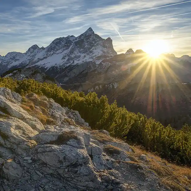 Ein atemberaubender Sonnenaufgang hinter der Gipfelspitze eines Berges, der den Himmel in warmen Farben erleuchtet und die Berglandschaft in goldenes Licht taucht.