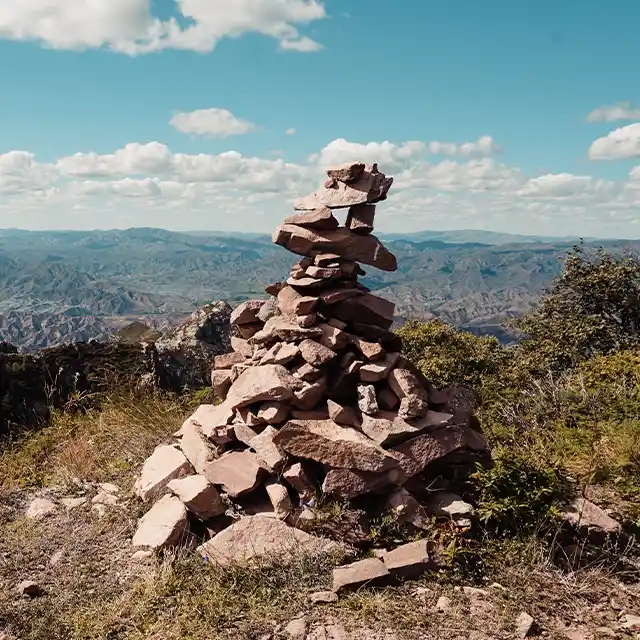 Ein beeindruckender Blick ins Tal, mit einer locker gestapelten Pyramide aus unterschiedlich großen Steinen am Rand eines Abgrunds.