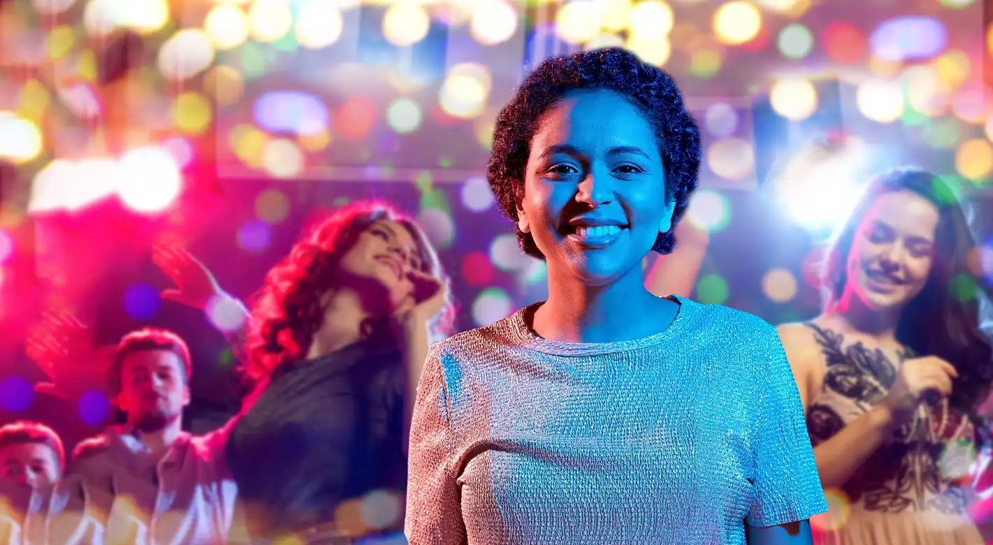 Eine Frau trifft sich mit Freundinnen zur sommerlichen Partynacht. Im Hintergrund ist ein kunterbuntes Lichtermeer, welches durch den Bokeh-Effekt die ausgelassene Stimmung unterstreicht.