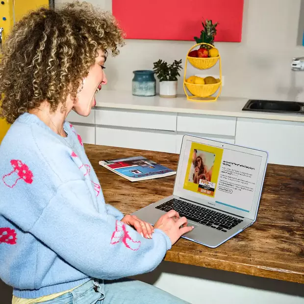 Eine gut gelaunte Frau sitzt entspannt am Laptop und blickt begeistert auf die ORWO Testurteile. Das Bild vermittelt eine positive Atmosphäre und zeigt die Freude über die Qualität der Fotoprodukte.