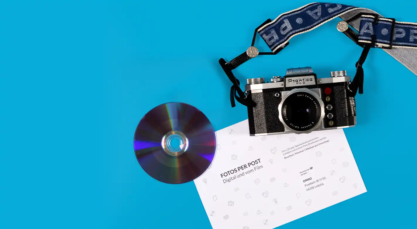 Kamera, CD und ORWO Versandumschlag auf gelbem Hintergrund